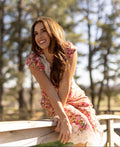 Woman in a floral dress sitting on a wooden railing with trees in the background