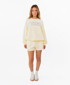 A woman modeling a butter yellow lounge set consisting of a sweatshirt with 'KITTENISH' printed in white across the chest and matching shorts, styled with white socks and white sneakers against a plain white background.