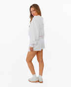 A woman modeling a white zip-up hoodie and matching white drawstring shorts, photographed against a solid white background.