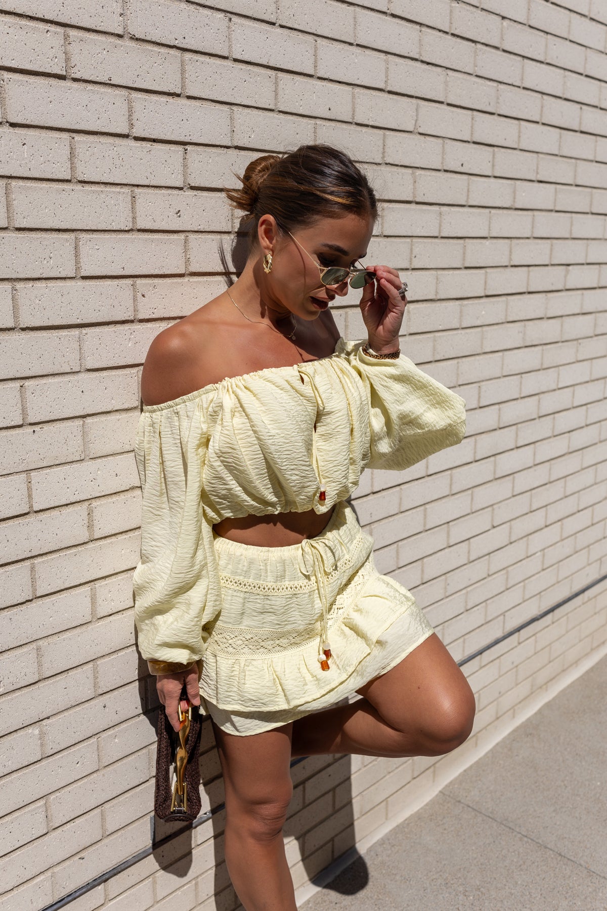 Jessie in a light yellow outfit standing against a white brick wall.