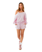 A woman modeling a light pink two-piece lounge set consisting of a cropped zip-up hoodie and matching drawstring shorts, paired with white socks and pink sneakers, against a solid white background.