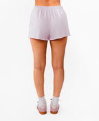 A model from the waist down wearing light pink drawstring shorts, white socks, and matching pink sneakers against a plain white background.