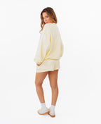 A woman modeling a pale yellow sweatshirt and matching shorts set against a plain white background. The sweatshirt features the word 'KITTENISH' in a white arched font outlined in black across the chest.