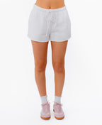 White drawstring shorts worn by a model, paired with white socks and pink sneakers, shown from the waist down on a plain white studio background.