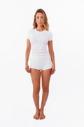 Model wearing a white short-sleeve ribbed top and matching white shorts against a plain white studio background.