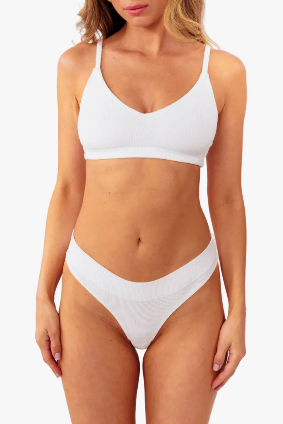 A model wearing a white ribbed thong standing against a plain white background.