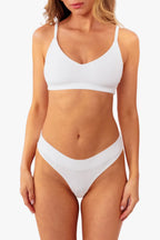 A model wearing a white ribbed thong standing against a plain white background.