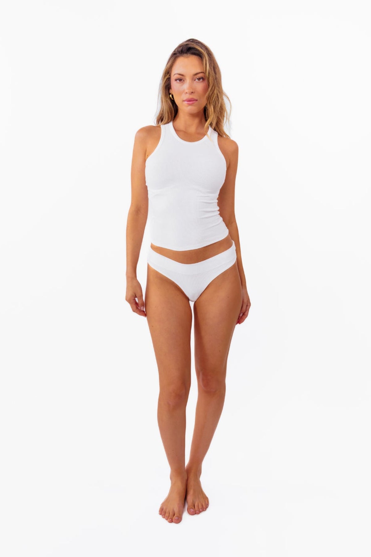 Model wearing a white ribbed tank top and matching white thong against a plain white background.