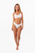 A model wearing a white ribbed thong standing against a plain white background.