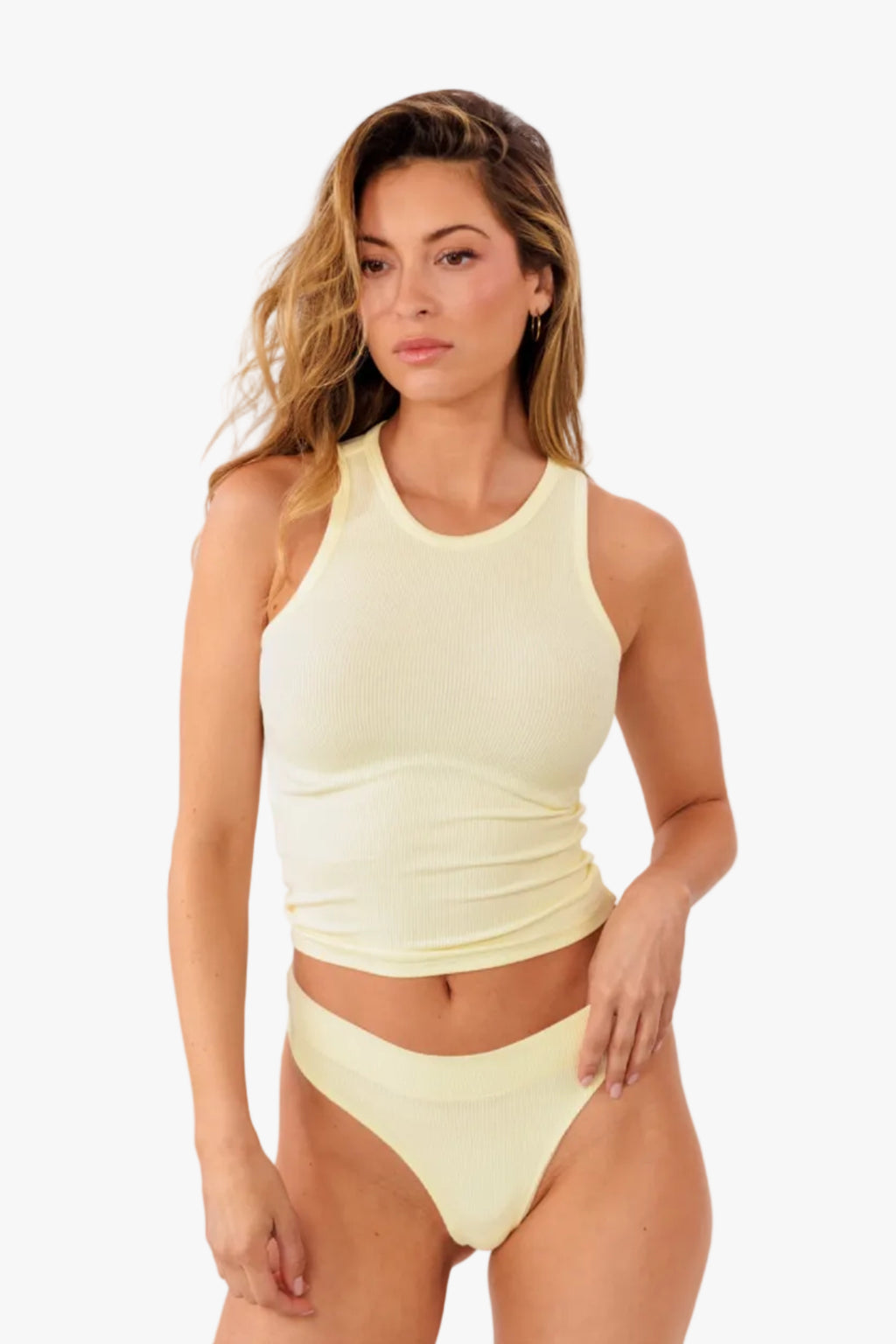 Model wearing pale yellow ribbed tank top and matching thong standing against a solid white background.