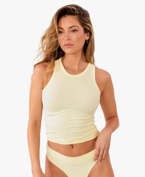 Model wearing pale yellow ribbed tank top and matching thong standing against a solid white background.