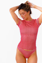 A woman modeling a red and white gingham tee and thong against a plain white background.