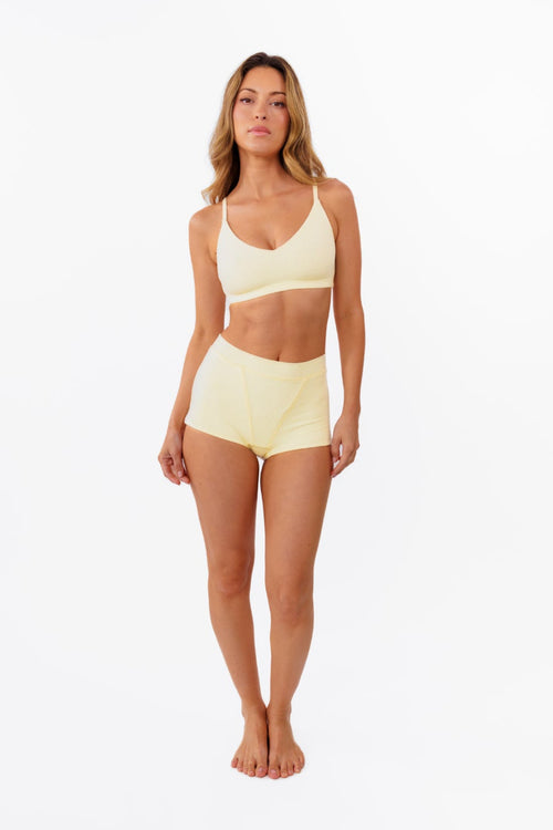 model wearing butter yellow boyshorts with matching bralette standing in front of a white backdrop