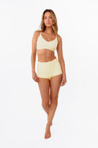 model wearing butter yellow boyshorts with matching bralette standing in front of a white backdrop