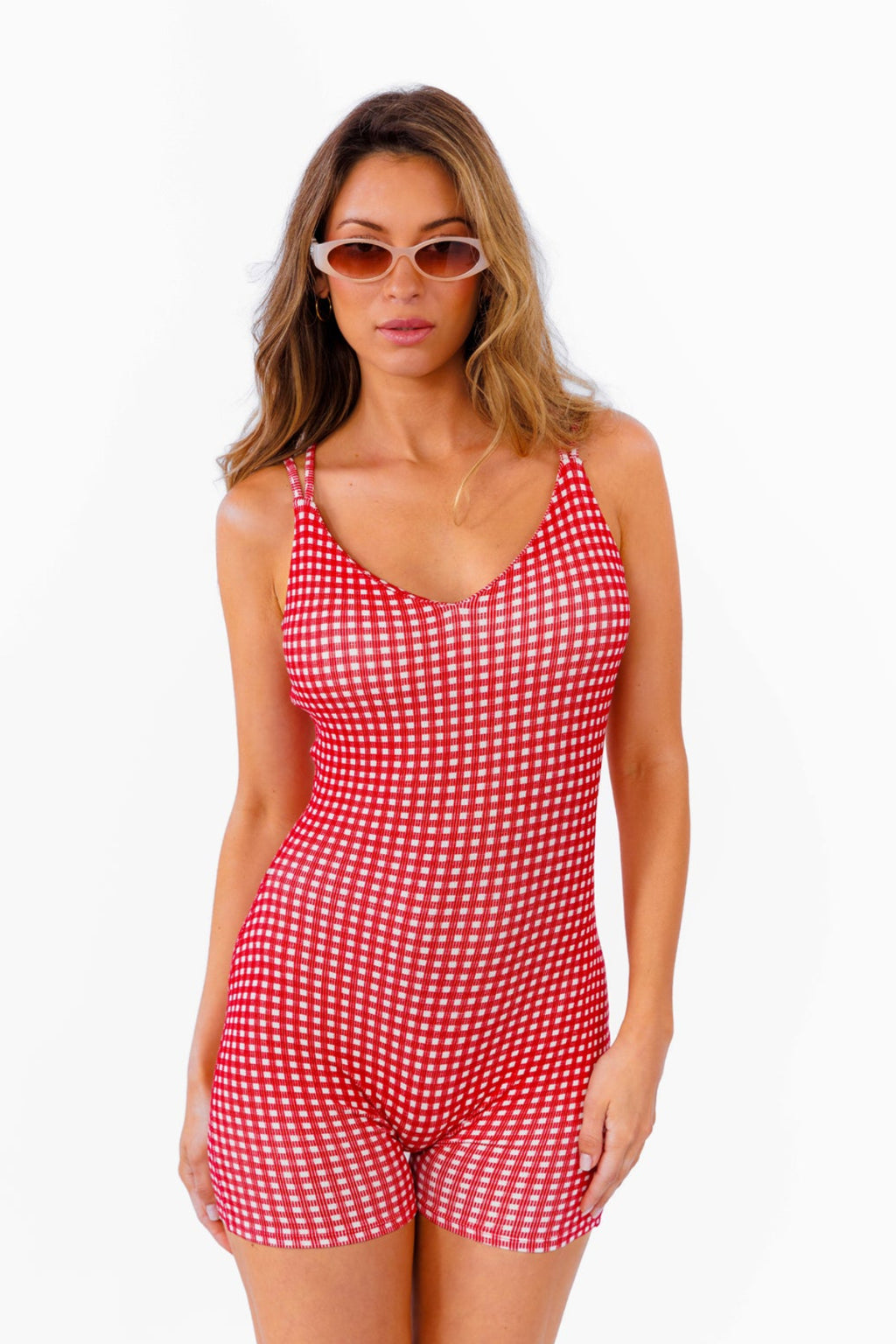 A woman modeling a red and white gingham patterned fitted romper against a plain white background.