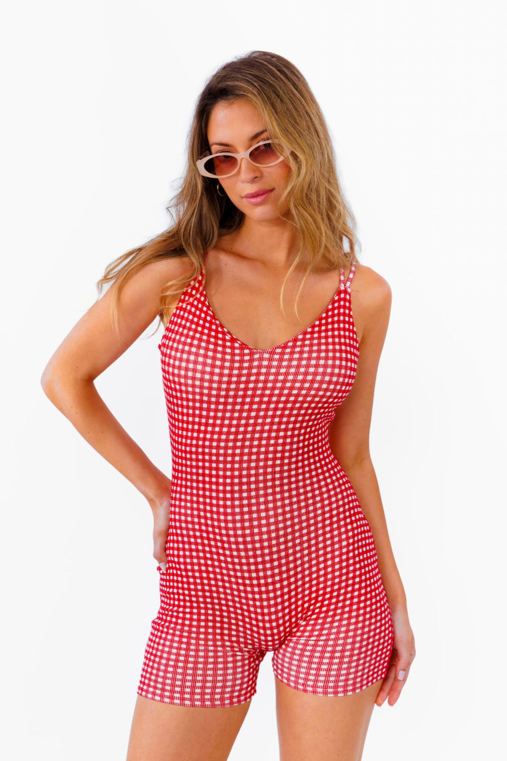 A woman modeling a red and white gingham patterned fitted romper against a plain white background.