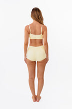 model wearing butter yellow boyshorts with matching bralette standing in front of a white backdrop