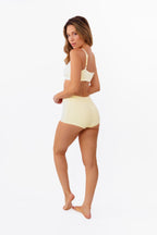 A model wearing pale yellow high-waisted ribbed boyshorts and matching bralette