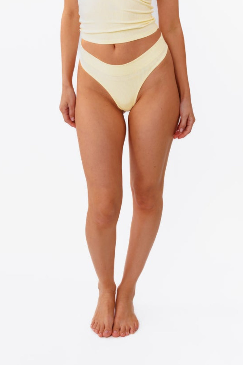 A model wearing a pale yellow ribbed thong and matching top, shown from the waist down against a plain white background.