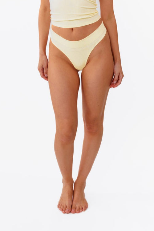 A model wearing a pale yellow ribbed thong and matching top, shown from the waist down against a plain white background.