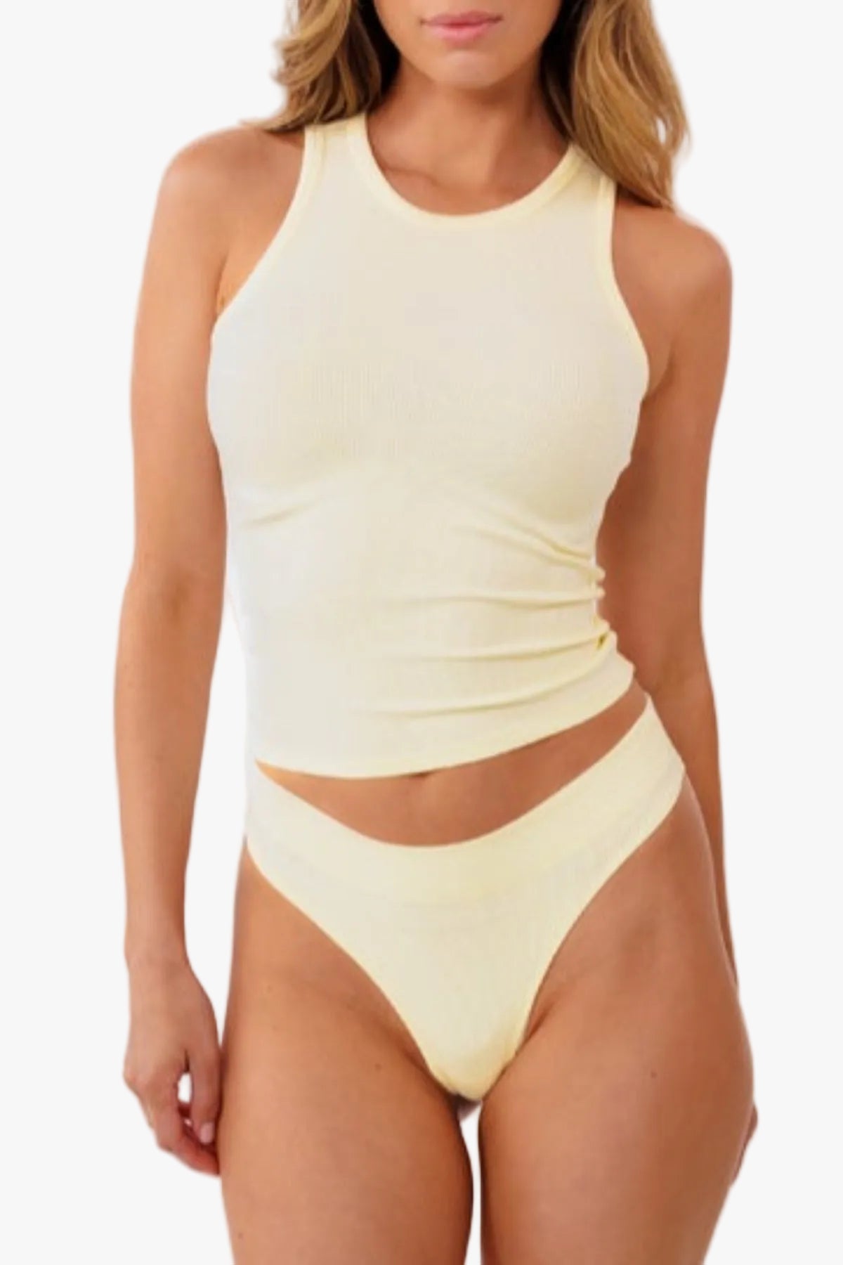 Model wearing pale yellow ribbed tank top and matching thong standing against a solid white background.