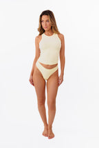 Model wearing pale yellow ribbed tank top and matching thong standing against a solid white background.