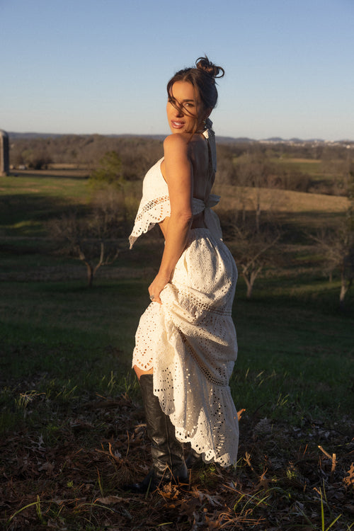 Woman in a white outfit standing in a field with a scenic background