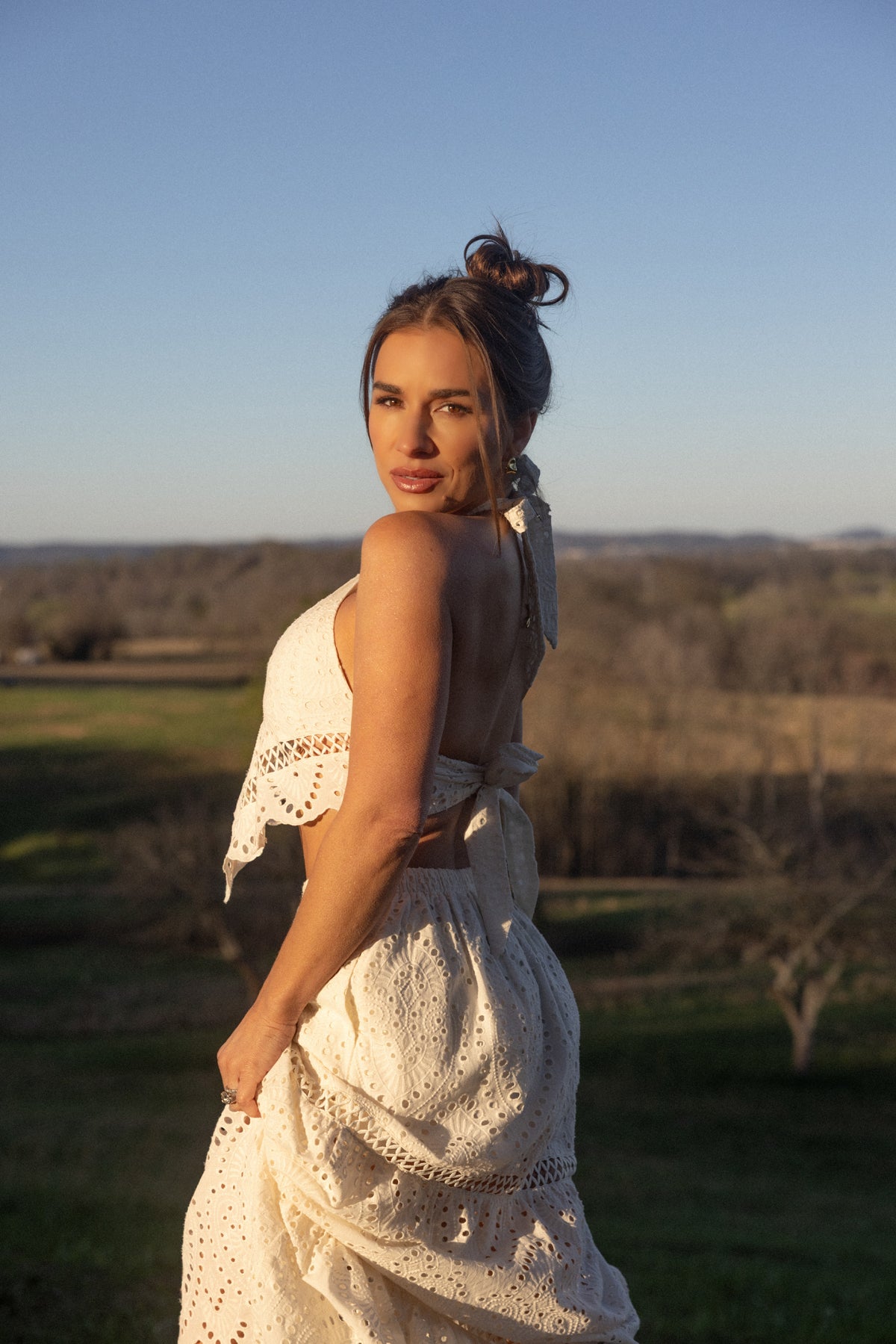 Woman in a white outfit standing in a field with a clear blue sky.