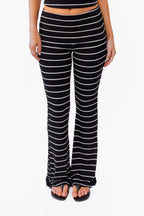 A woman modeling a black and white  two-piece lounge set with horizontal striped textures, consisting of a v neck tank top and matching fold over flared pant, against a plain white background.