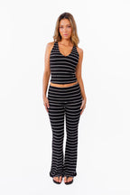 A woman modeling a black and white  two-piece lounge set with horizontal striped textures, consisting of a v neck tank top and matching fold over flared pant, against a plain white background.