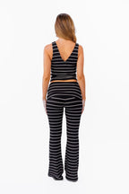 A woman modeling a black and white  two-piece lounge set with horizontal striped textures, consisting of a v neck tank top and matching fold over flared pant, against a plain white background.