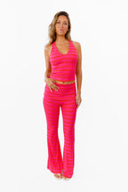 A woman modeling a bright pink two-piece lounge set with horizontal striped textures, consisting of a v neck tank top and matching flared pants with a fold over waistband, against a plain white background.
