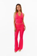 A woman modeling a bright pink two-piece lounge set with horizontal striped textures, consisting of a v neck tank top and matching flared pants with a fold over waistband, against a plain white background.