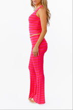 A woman modeling a bright pink two-piece lounge set with horizontal striped textures, consisting of a v neck tank top and matching flared pants with a fold over waistband, against a plain white background.