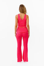 A woman modeling a bright pink two-piece lounge set with horizontal striped textures, consisting of a v neck tank top and matching flared pants with a fold over waistband, against a plain white background.