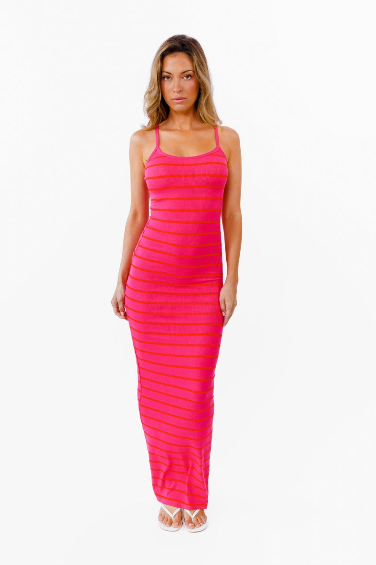 A woman modeling a bright pink and red striped sleeveless, horizontally striped maxi dress against a plain white background.