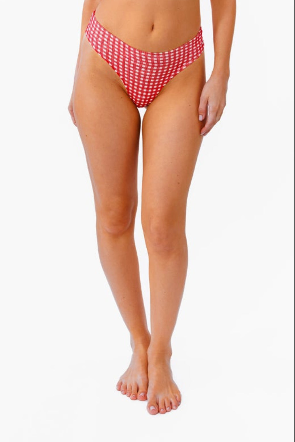 A woman modeling a red and white gingham bralette and thong against a plain white background.