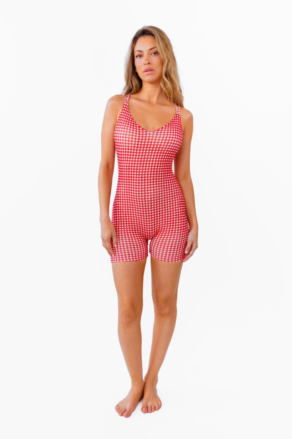 A woman modeling a red and white gingham patterned fitted romper against a plain white background.