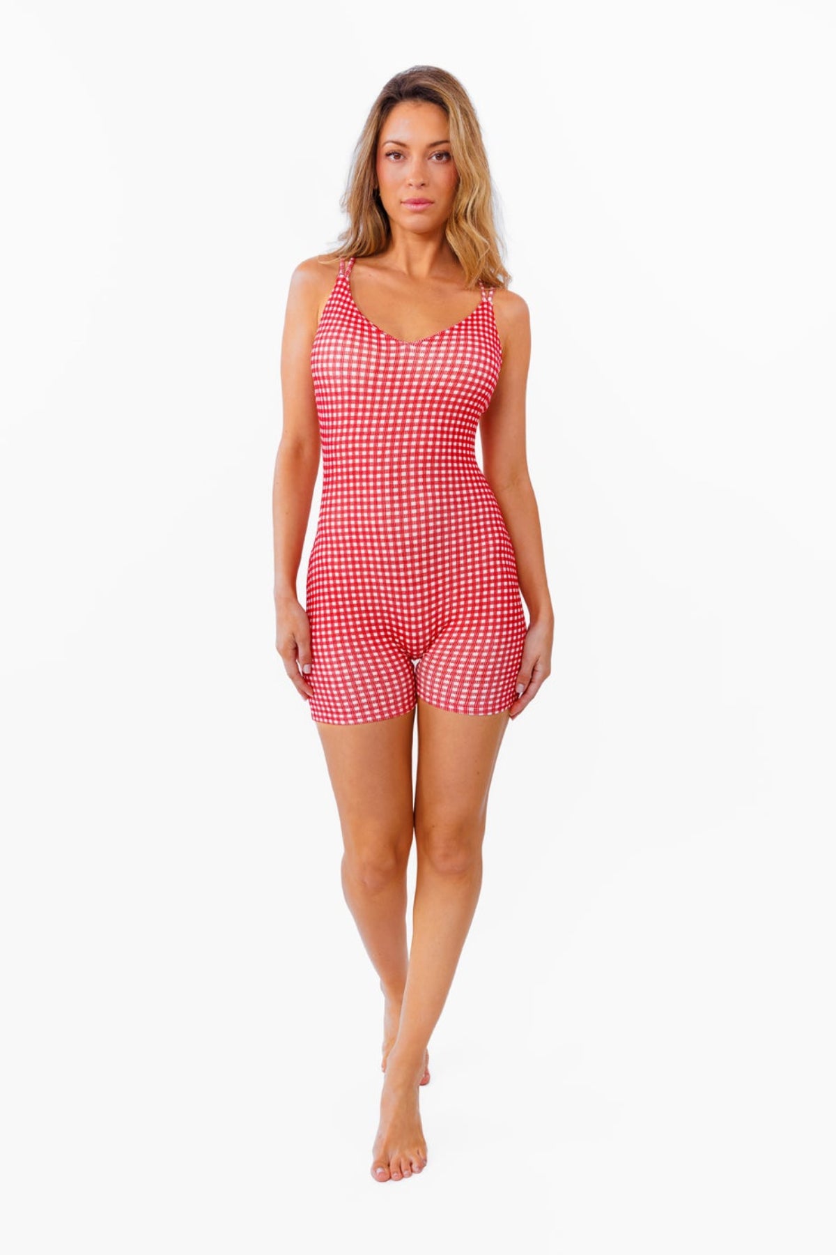 A woman modeling a red and white gingham patterned fitted romper against a plain white background.