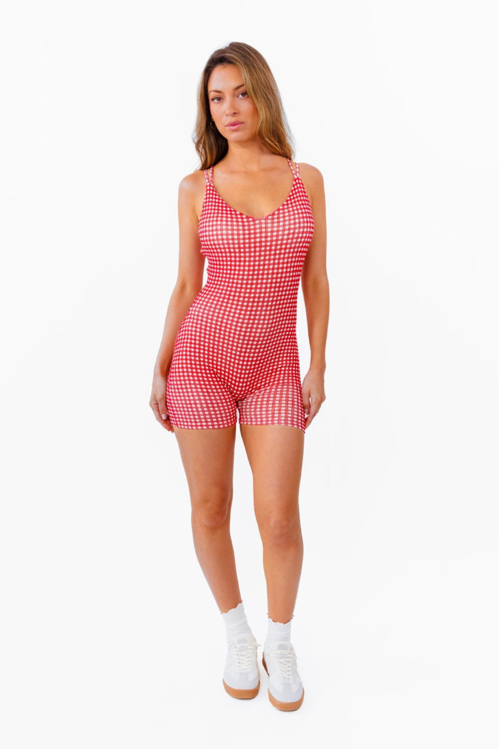 A woman modeling a red and white gingham patterned fitted romper against a plain white background.