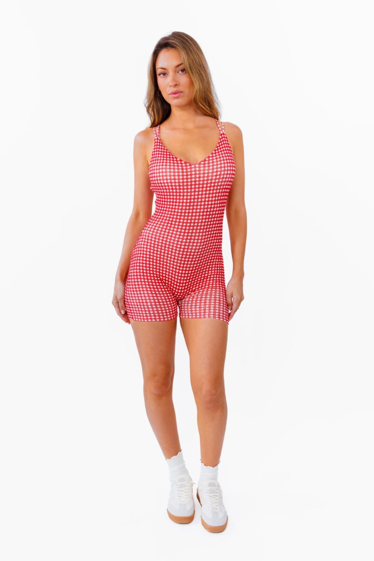 A woman modeling a red and white gingham patterned fitted romper against a plain white background.