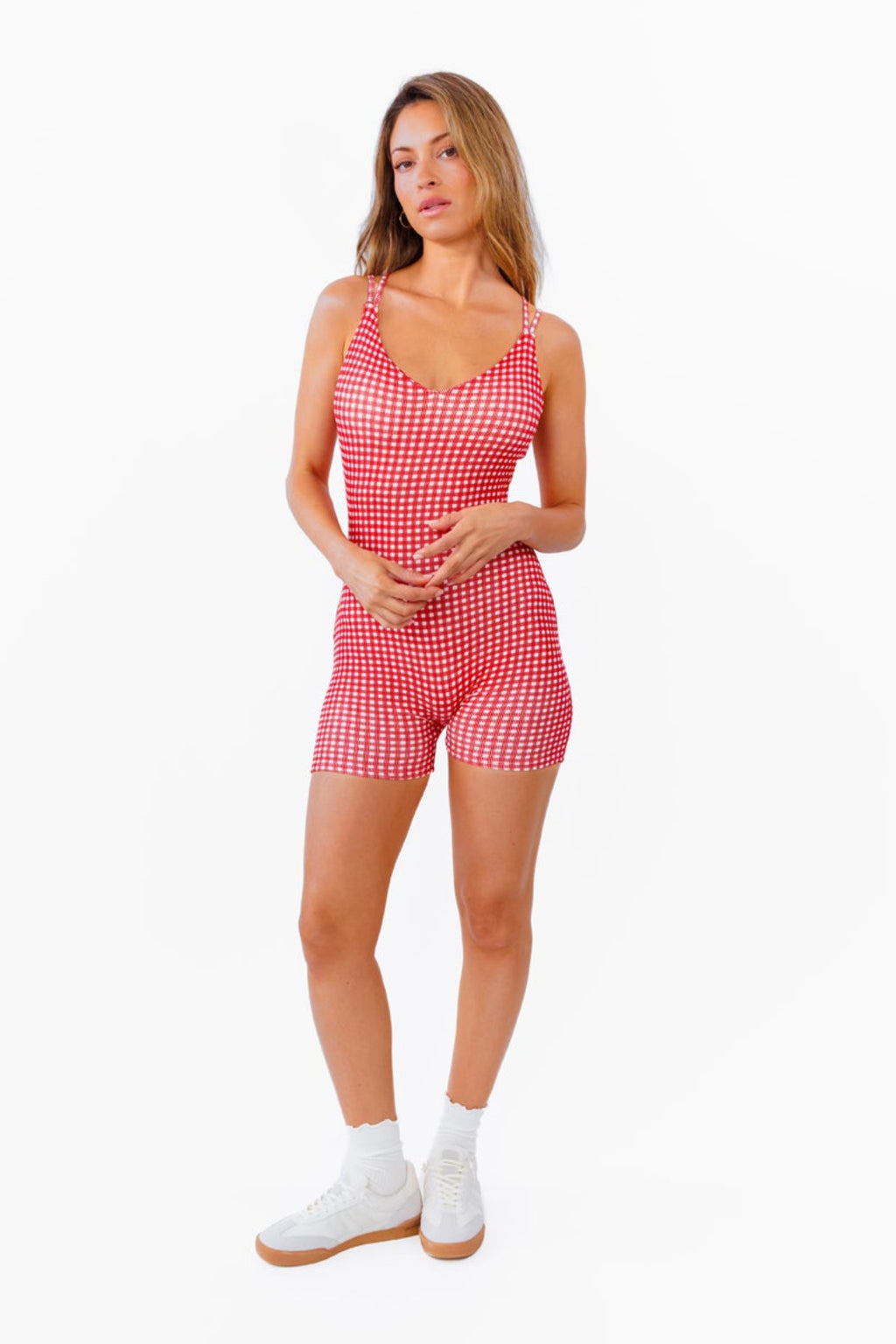 A woman modeling a red and white gingham patterned fitted romper against a plain white background.