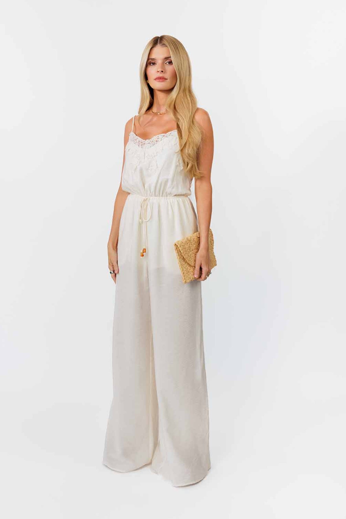 Woman wearing a white jumpsuit with a beige clutch against a white background