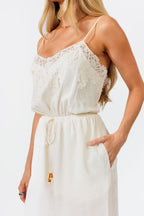 Woman wearing a white lace jumpsuit against a plain background