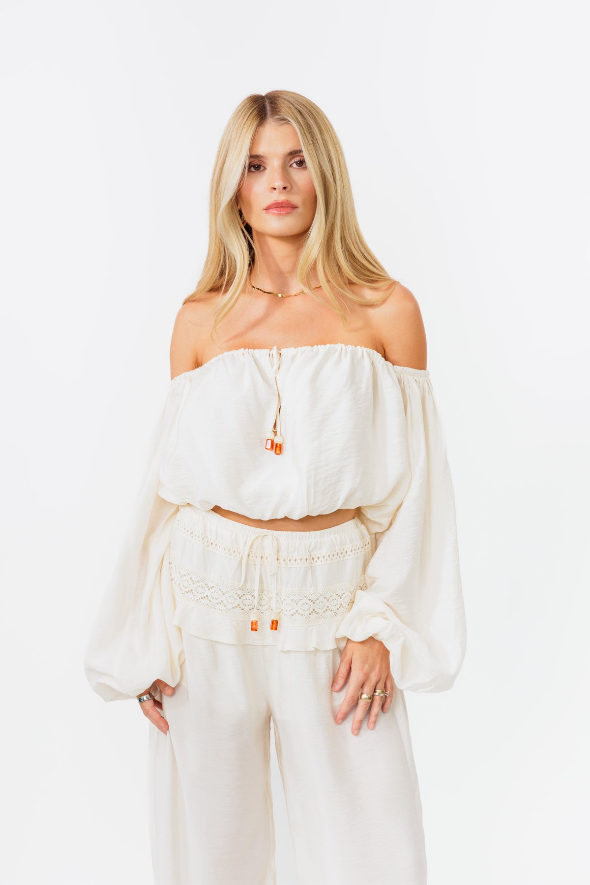 Woman wearing a white off-shoulder top and pants on a white background
