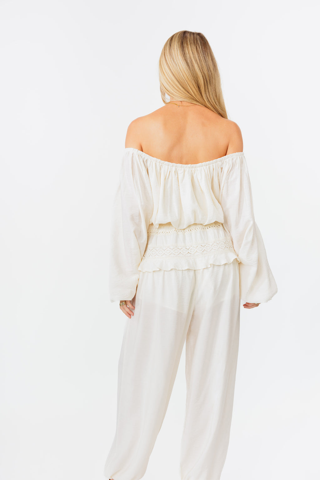 Woman wearing a white off-shoulder top and pants on a white background