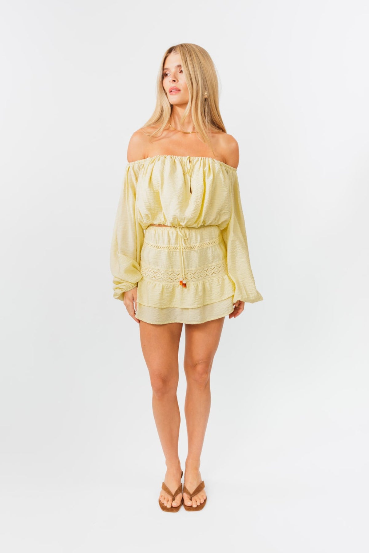 Woman wearing a light yellow off-shoulder top and skirt set on a white background