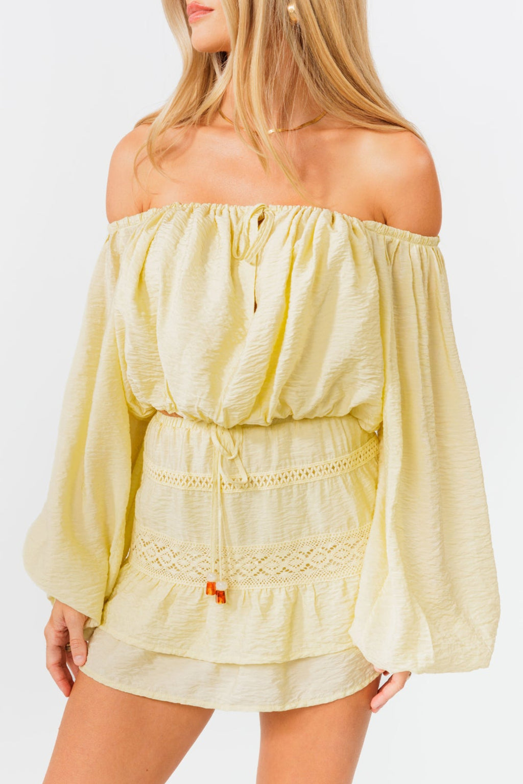 Woman wearing a light yellow off-shoulder top and skirt set on a white background