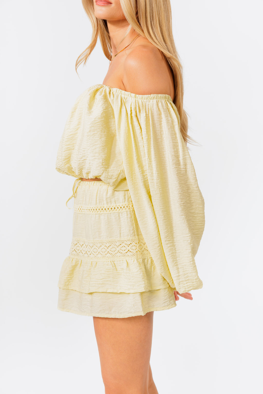 Woman wearing a light yellow off-shoulder top and skirt set on a white background