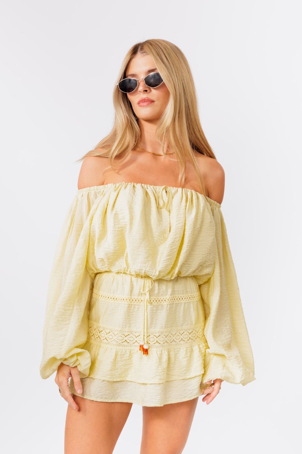 Woman wearing a light yellow off-shoulder top and skirt set on a white background